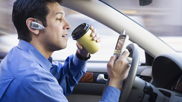 Hispanic businessman using cell phone drinking coffee and driving